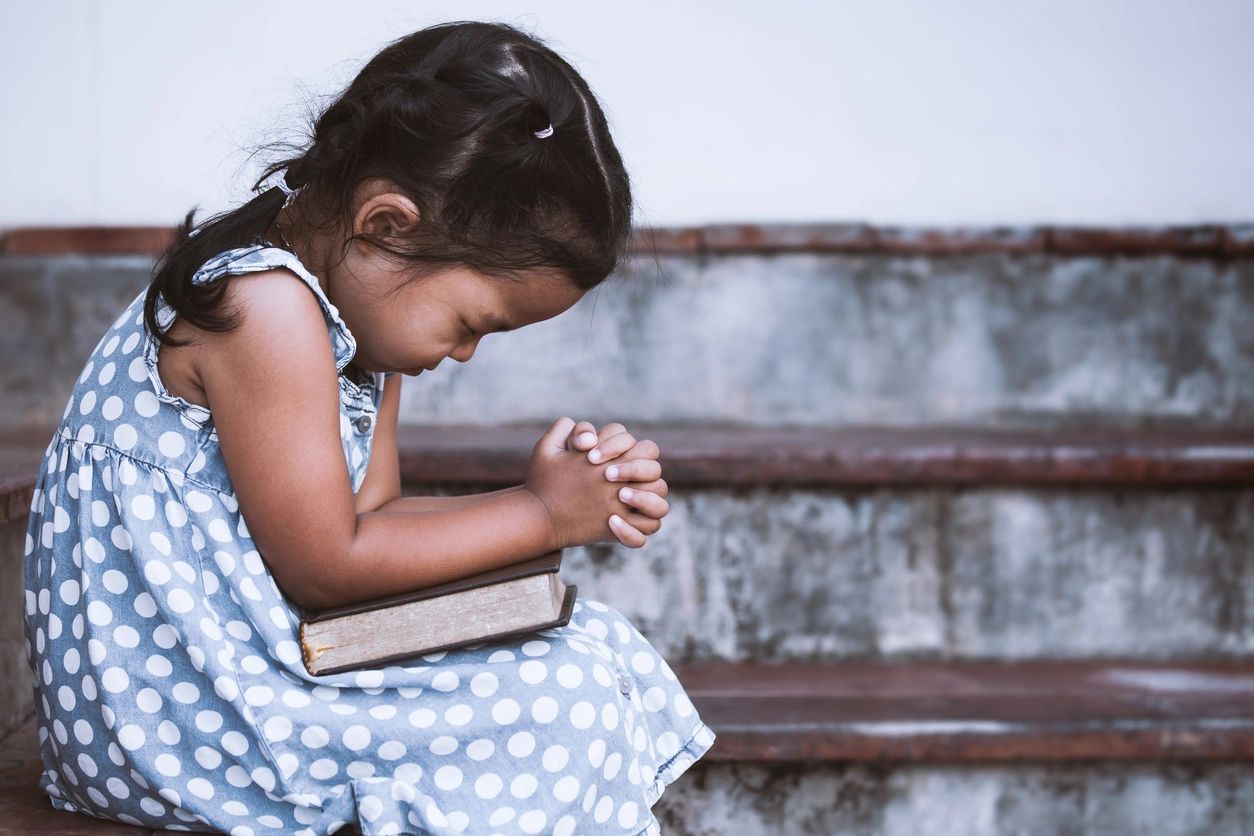 Young girl sitting along praying with bible in her lap. Grace Place Transitional Housing and Support for Single Mothers Experiencing Homelessness in Sumner County, TN - How Your Gift Helps Families Find Shelter and Stability
